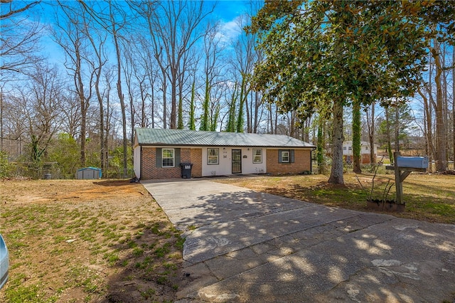 ranch-style house featuring an outbuilding, a shed, concrete driveway, metal roof, and brick siding