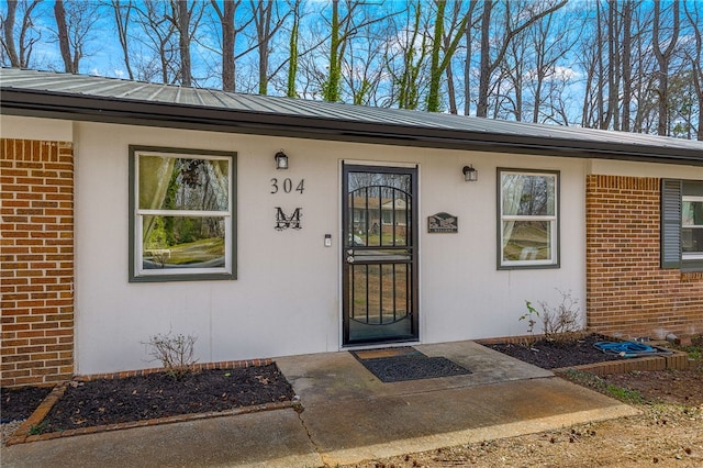 doorway to property with metal roof, brick siding, and a standing seam roof