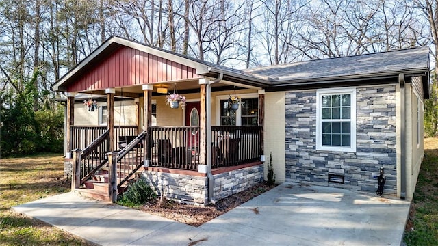 view of front of house featuring stone siding, covered porch, and board and batten siding