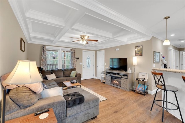 living room with light wood-style flooring, ornamental molding, coffered ceiling, a glass covered fireplace, and baseboards