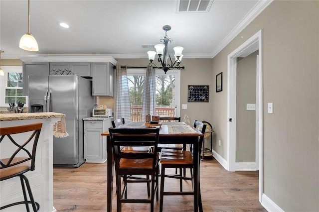 dining room featuring crown molding, baseboards, visible vents, and light wood finished floors