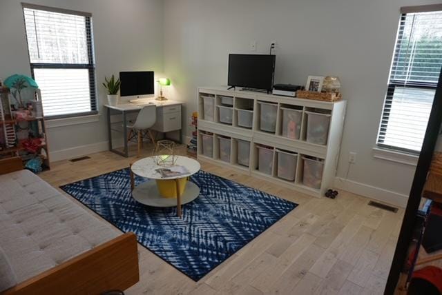 living area with a wealth of natural light, visible vents, baseboards, and wood finished floors