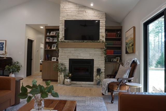 living area with a wealth of natural light, a stone fireplace, wood finished floors, and vaulted ceiling