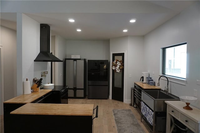 kitchen with refrigerator, freestanding refrigerator, a sink, exhaust hood, and butcher block counters