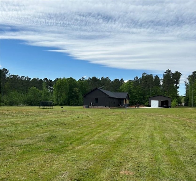 view of yard featuring an outbuilding, a wooded view, driveway, a pole building, and a detached garage