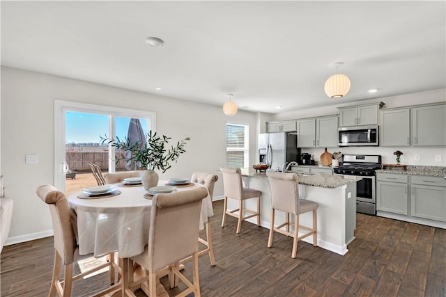 kitchen featuring dark wood finished floors, stainless steel appliances, an island with sink, and light stone counters