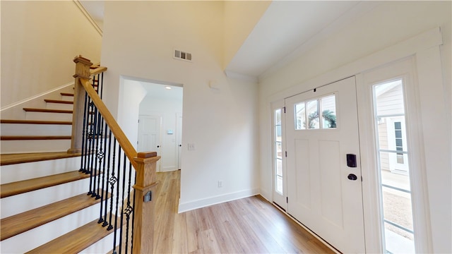 entrance foyer featuring visible vents, light wood-style floors, a high ceiling, baseboards, and stairs