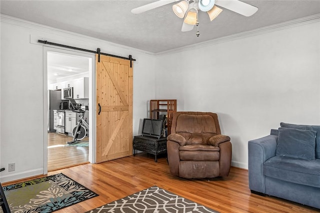 living area featuring a barn door, a ceiling fan, wood finished floors, and crown molding