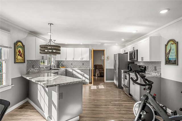 kitchen featuring a sink, wood finished floors, white cabinetry, stainless steel appliances, and a peninsula