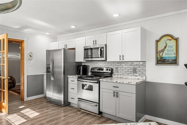 kitchen with backsplash, baseboards, light stone counters, wood finished floors, and stainless steel appliances