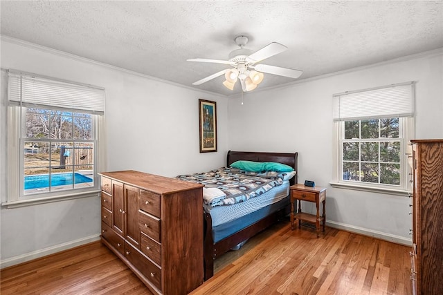 bedroom with light wood finished floors, a textured ceiling, baseboards, and ornamental molding