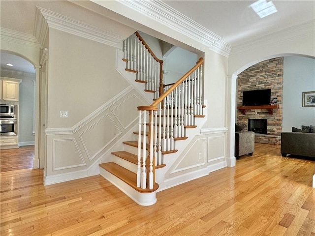 stairway featuring a decorative wall, ornamental molding, a stone fireplace, and wood finished floors