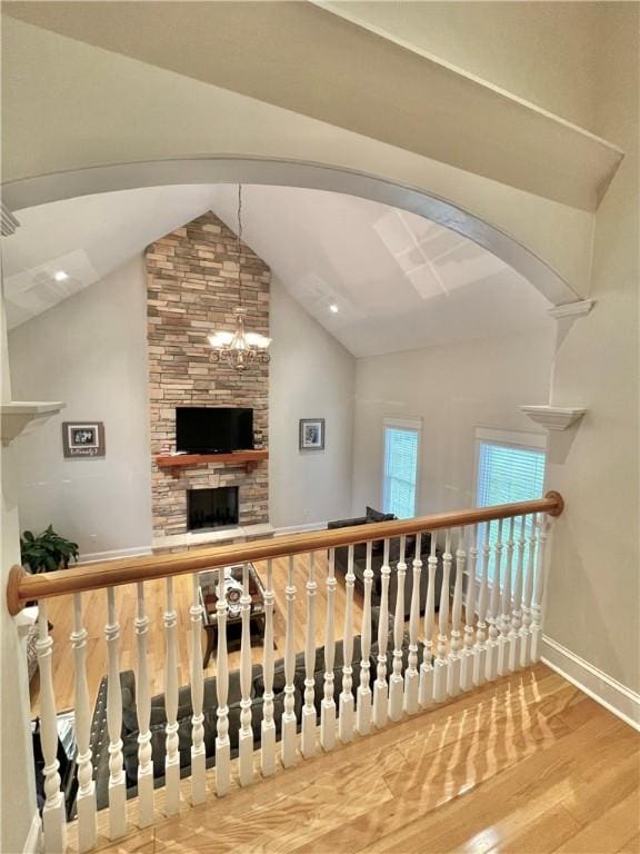 staircase with wood finished floors, baseboards, arched walkways, lofted ceiling, and a chandelier