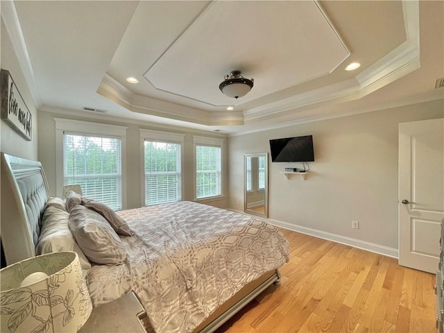 bedroom with light wood-type flooring, visible vents, a raised ceiling, crown molding, and baseboards