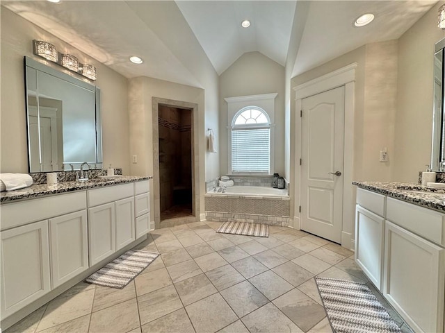 bathroom featuring a garden tub, two vanities, a sink, a spacious closet, and vaulted ceiling