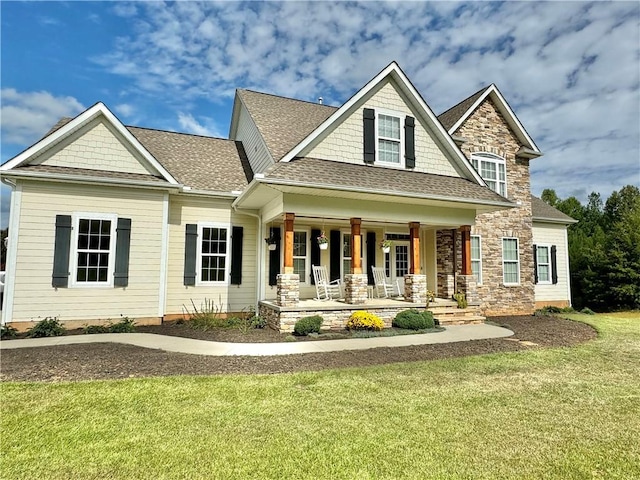 craftsman house featuring stone siding, roof with shingles, a porch, and a front yard