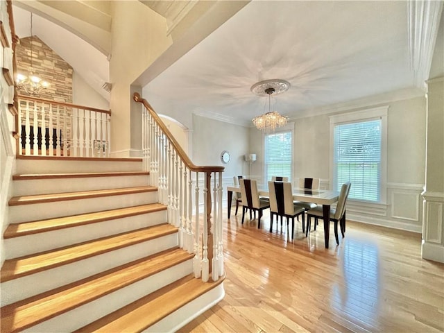 dining space featuring stairway, wood finished floors, an inviting chandelier, ornamental molding, and a decorative wall