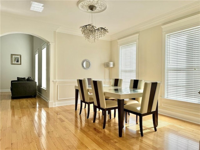 dining room with arched walkways, a chandelier, light wood finished floors, and crown molding