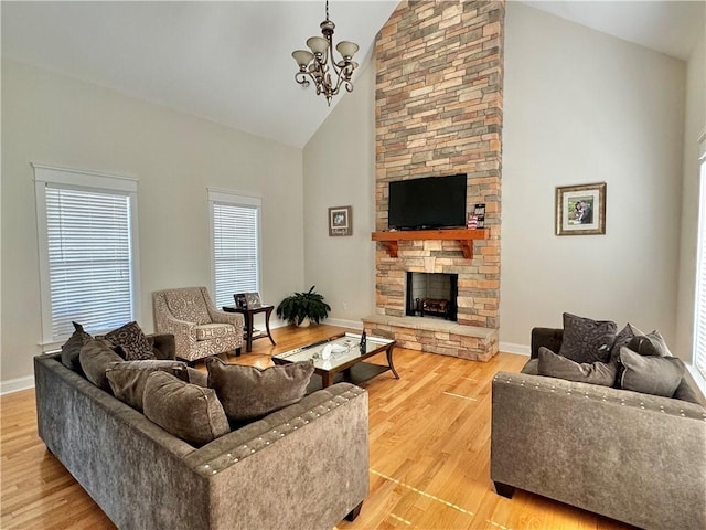 living area featuring baseboards, a chandelier, light wood-type flooring, a stone fireplace, and high vaulted ceiling