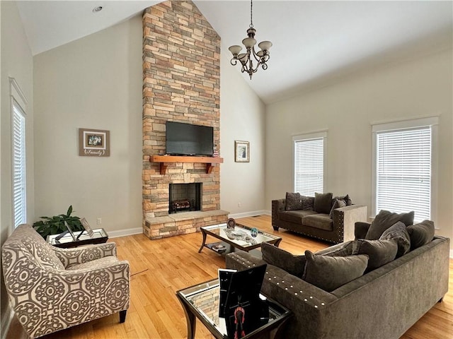 living room with a notable chandelier, high vaulted ceiling, wood finished floors, a stone fireplace, and baseboards