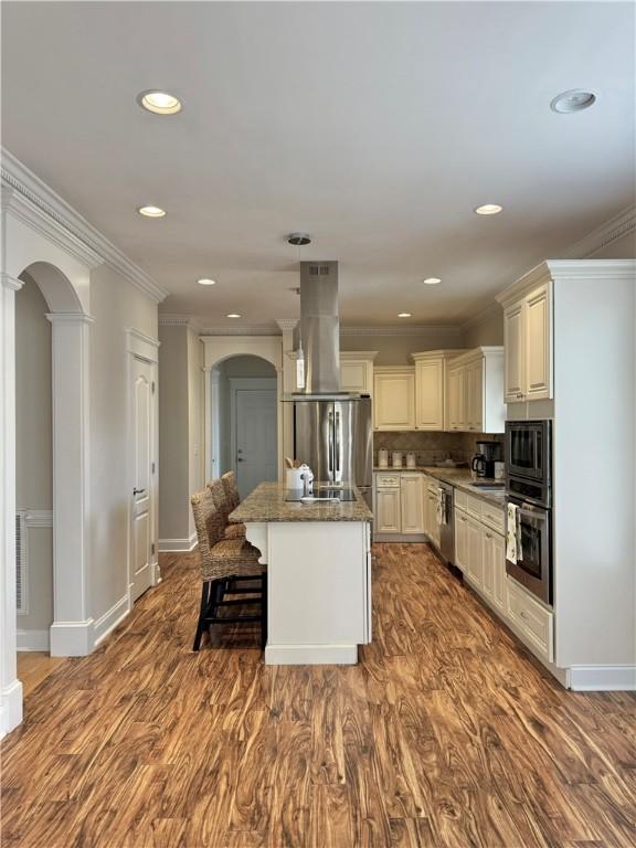 kitchen with arched walkways, ornamental molding, appliances with stainless steel finishes, and island range hood