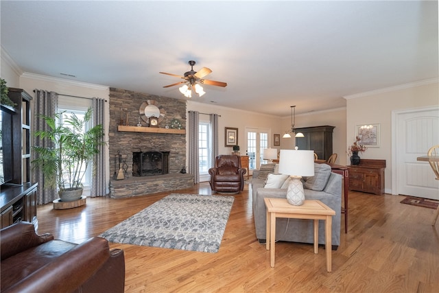 living room featuring light wood-type flooring, a stone fireplace, and crown molding