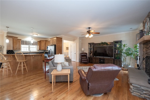 living room with a ceiling fan, a fireplace, light wood finished floors, and ornamental molding