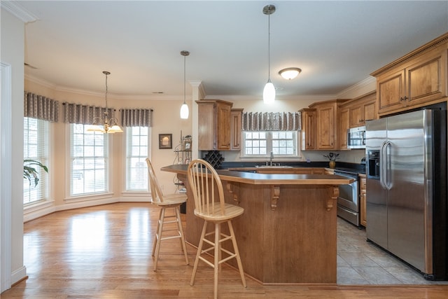 kitchen with a breakfast bar area, a peninsula, brown cabinetry, stainless steel appliances, and a sink