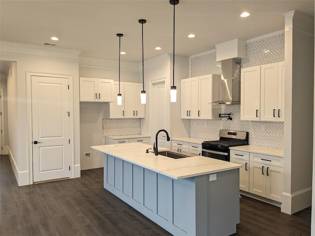 kitchen with dark wood-type flooring, stainless steel range with gas cooktop, wall chimney range hood, white cabinets, and a sink