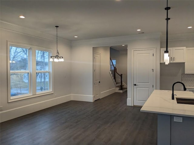 unfurnished dining area featuring dark wood-style floors, baseboards, ornamental molding, stairs, and a sink