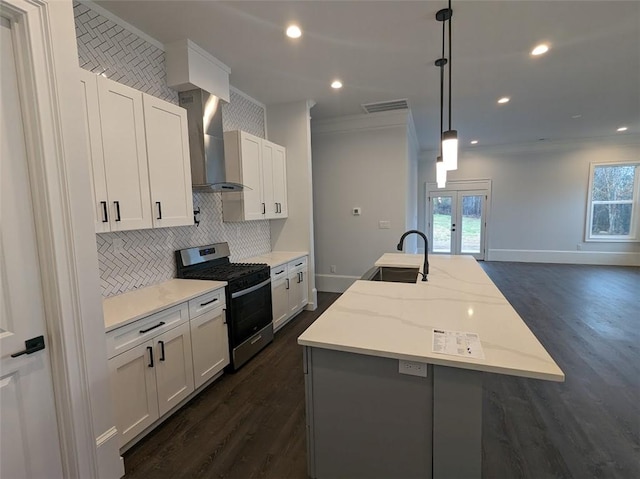 kitchen featuring visible vents, an island with sink, a sink, wall chimney range hood, and stainless steel gas range