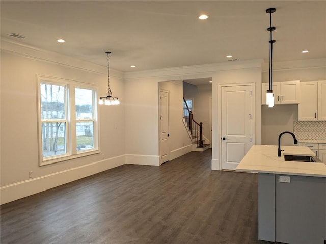 kitchen featuring light stone countertops, dark wood finished floors, ornamental molding, decorative backsplash, and a sink