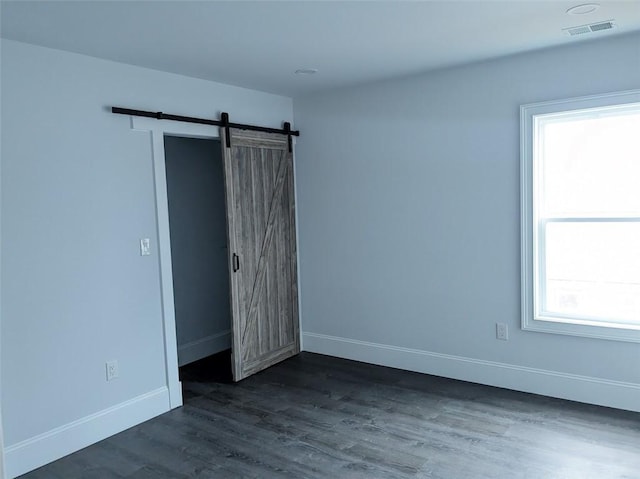 unfurnished bedroom featuring a barn door, baseboards, visible vents, and dark wood-style floors