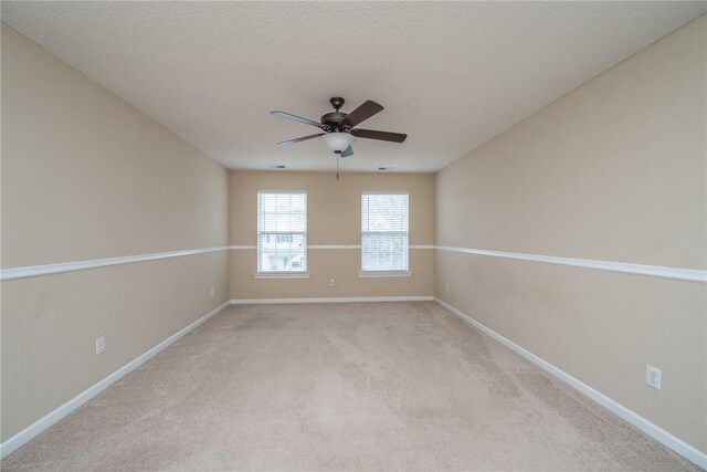 empty room with light colored carpet, a textured ceiling, baseboards, and ceiling fan