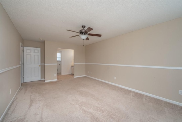 spare room with baseboards, light colored carpet, a ceiling fan, and a textured ceiling