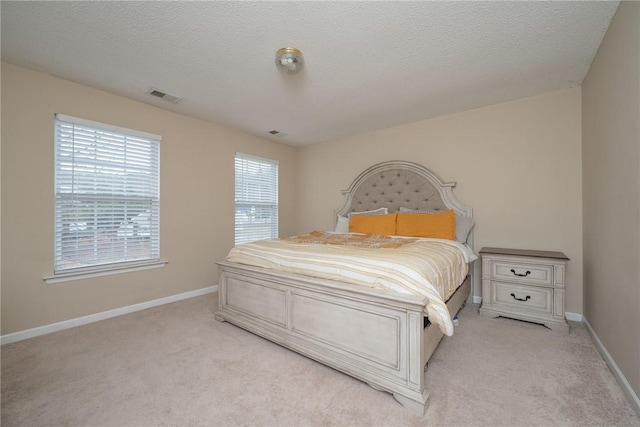 bedroom with a textured ceiling, light colored carpet, visible vents, and baseboards