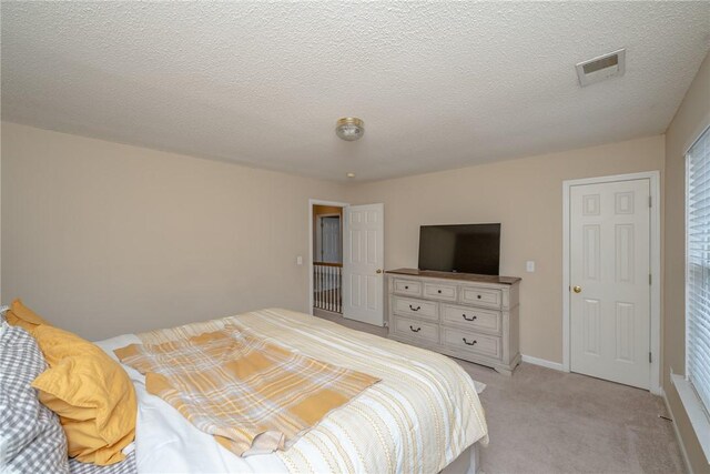 bedroom featuring a textured ceiling, light colored carpet, visible vents, and baseboards