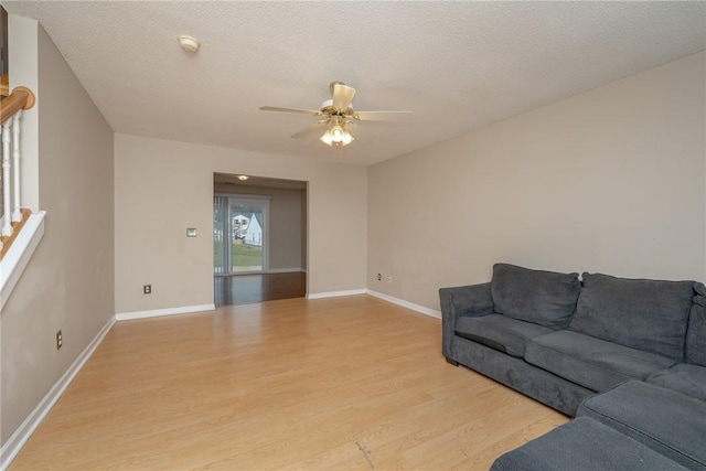 living room with baseboards, light wood-style floors, ceiling fan, and a textured ceiling