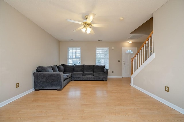 living room with baseboards, a ceiling fan, stairs, and light wood finished floors