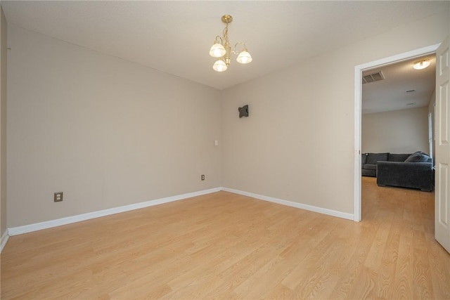 spare room with an inviting chandelier, light wood-style flooring, baseboards, and visible vents