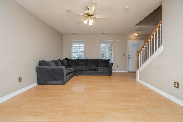 living area with stairway, baseboards, ceiling fan, and light wood finished floors