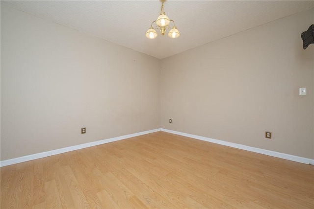 empty room with a chandelier, baseboards, and light wood-style floors