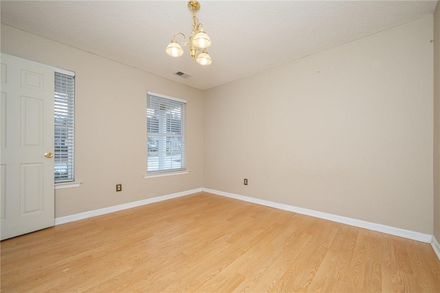 spare room with light wood-style flooring, a notable chandelier, baseboards, and visible vents