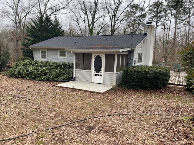 back of house featuring a patio area, a shingled roof, a chimney, and a sunroom