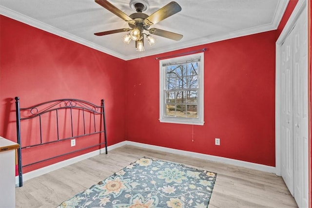 bedroom with crown molding, wood finished floors, a closet, and baseboards