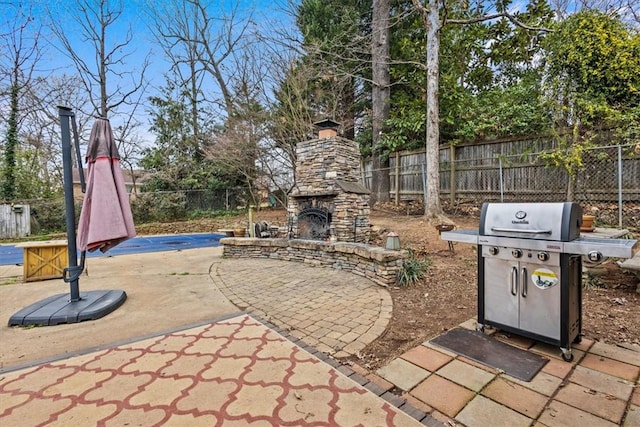 view of patio with grilling area, an outdoor stone fireplace, and fence