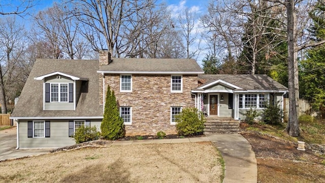 tri-level home featuring stone siding, roof with shingles, and a chimney