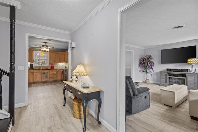 living area with visible vents, crown molding, baseboards, light wood-type flooring, and a textured ceiling