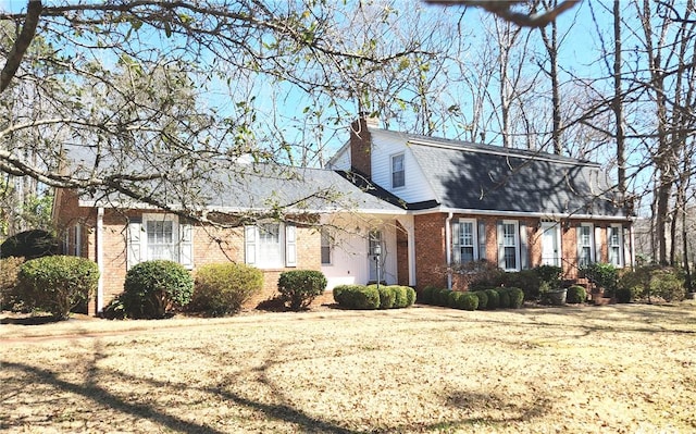 colonial inspired home featuring a gambrel roof, brick siding, and roof with shingles