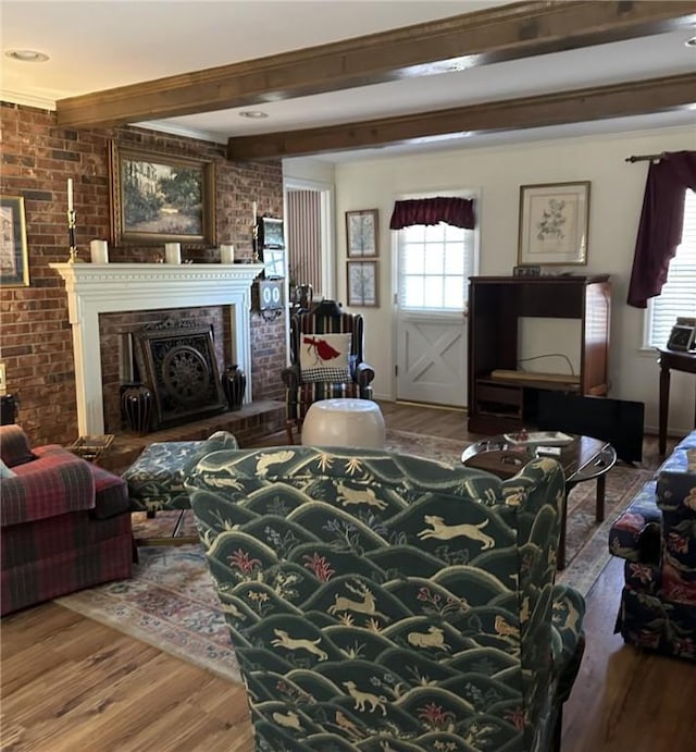 living area with a fireplace, beamed ceiling, wood finished floors, and brick wall